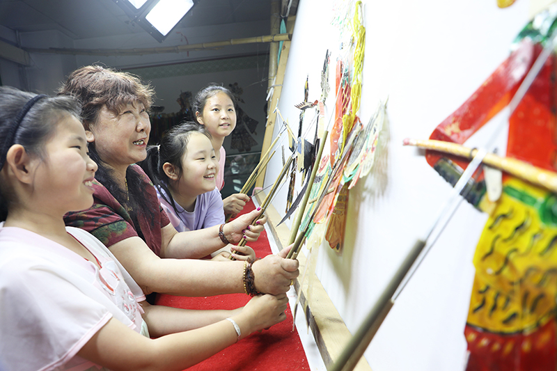 皮影藝人指導(dǎo)小朋友表演皮影戲。