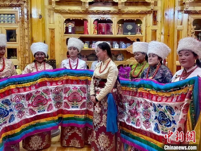 圖為女性展示村民自發(fā)繡制的“百米五彩哈達”?！±钣穹?攝
