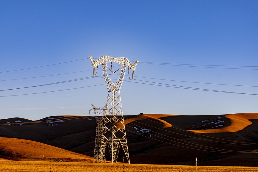 阿里地區(qū)的曠野上，電力鐵塔在夕陽下熠熠生輝。